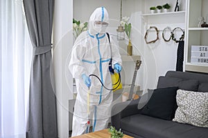 A medical staff in PPE suit is using disinfectant spray in living room, Covid-19 protection , disinfection concept