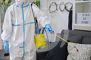 Medical staff in PPE suit is using disinfectant spray in living room, Covid-19 protection , disinfection concept