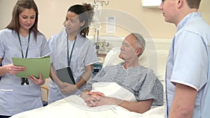 Medical Staff On Rounds Standing By Female Patient's Bed