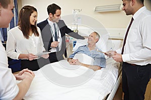 Medical Staff On Rounds Standing By Male Patient's Bed