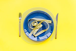 Medical starvation for lose weight. Empty plate, apple and measuring tape on bright yellow background top view
