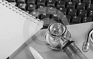 medical stethoscope on computer keyboard and ballpoint pen for notes