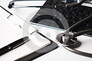 Medical stethoscope on computer keyboard with clipboard and pen