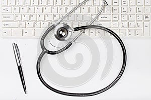 Medical stethoscope on computer keyboard with pen