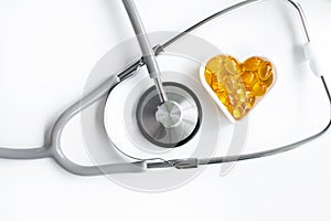 Medical stethoscope examining a heart listen to the rhythm on a white background with a heart shape with omega-3 capsules inside