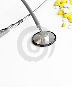 Medical stethoscope examining the heart listening to the rhythm on a white background with scattered yellow and white pills top