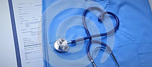 A medical stethoscope is intertwined in the shape of a heart and lies on a medical history and a blue uniform. Closeup