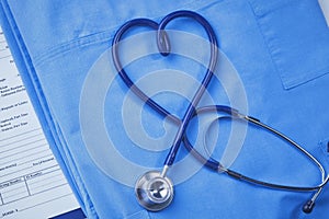 A medical stethoscope is intertwined in the shape of a heart and lies on a medical history and a blue uniform. Closeup