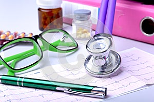 Medical stethoscope lying on cardiogram chart with pile of pills closeup. Cardiology care, health, protection