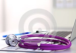 Medical stethoscope lying on a computer keyboard, cup of coffee