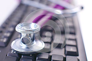 Medical stethoscope lying on a computer keyboard, documents