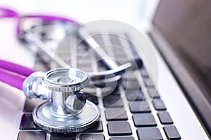 Medical stethoscope lying on a computer keyboard, documents