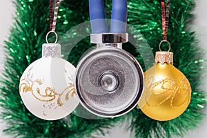 Medical stethoscope membrane anteriorly with two tubes surrounded by Christmas tree balls on blurred background with adornment. Co