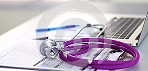 A medical stethoscope near a laptop on a wooden table, on white