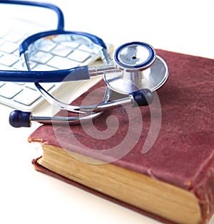 Medical stethoscope with old books and laptop on a table