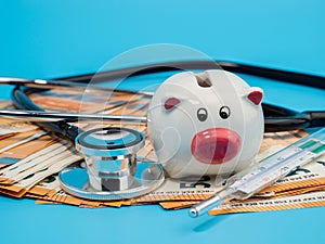 Medical stethoscope, piggy bank, thermometer and banknotes on a blue background.