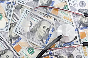 Medical stethoscope on a pile of money signifying the relationship of money and medicine.hundred dollar bills and a stethoscope