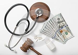 Medical stethoscope, pills, judge hammer and money on white back