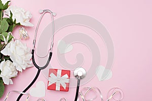 Medical stethoscope with red gift box, flowers roses and white hearts on pink background