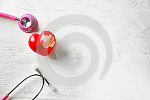 Medical stethoscope and red heart with plaster on white wooden background. Cardiology concept