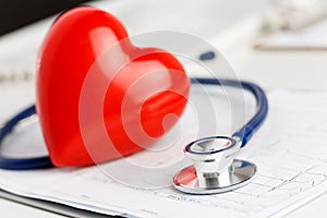 Medical stethoscope and red toy heart lying on cardiogram chart