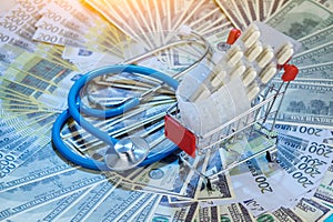 Medical stethoscope and shopping trolley on euro and dollar banknotes spread on table