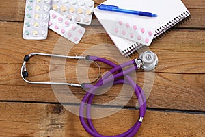 Medical stethoscope and tablets isolated on wooden background