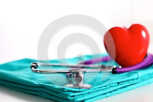 Medical stethoscope twisted in heart shape lying on patient medical history list and blue doctor uniform closeup