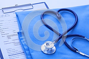 Medical stethoscope twisted in heart shape lying on patient medical history list and blue doctor uniform closeup