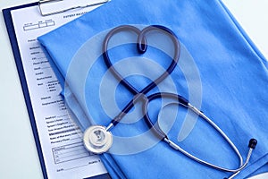 Medical stethoscope twisted in heart shape lying on patient medical history list and blue doctor uniform closeup