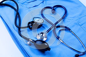 Medical stethoscope twisted in heart shape lying on patient medical history list and blue doctor uniform closeup