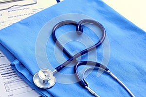 Medical stethoscope twisted in heart shape lying on patient medical history list and blue doctor uniform closeup