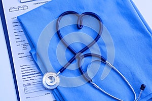 Medical stethoscope twisted in heart shape lying on patient medical history list and blue doctor uniform closeup