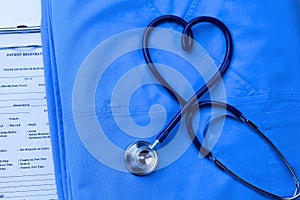 Medical stethoscope twisted in heart shape lying on patient medical history list and blue doctor uniform closeup