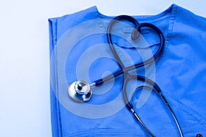 Medical stethoscope twisted in heart shape lying on patient medical history list and blue doctor uniform closeup