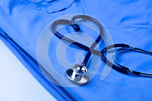 Medical stethoscope twisted in heart shape lying on patient medical history list and blue doctor uniform closeup