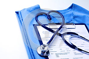 Medical stethoscope twisted in heart shape lying on patient medical history list and blue doctor uniform closeup