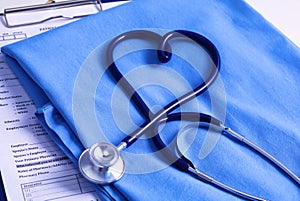 Medical stethoscope twisted in heart shape lying on patient medical history list and blue doctor uniform closeup