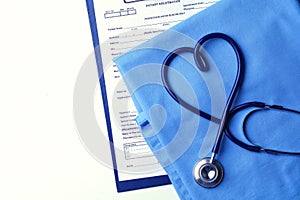 Medical stethoscope twisted in heart shape lying on patient medical history list and blue doctor uniform closeup