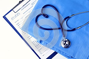 Medical stethoscope twisted in heart shape lying on patient medical history list and blue doctor uniform closeup