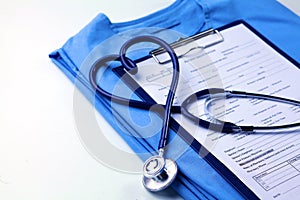 Medical stethoscope twisted in heart shape lying on patient medical history list and blue doctor uniform closeup