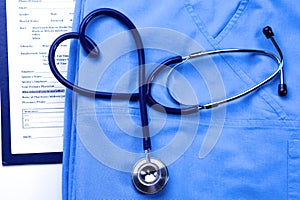 Medical stethoscope twisted in heart shape lying on patient medical history list and blue doctor uniform closeup