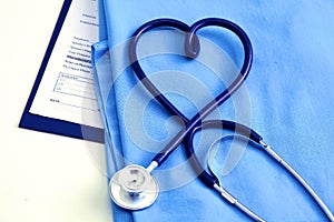 Medical stethoscope twisted in heart shape lying on patient medical history list and blue doctor uniform closeup