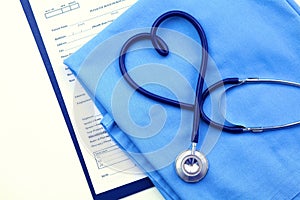 Medical stethoscope twisted in heart shape lying on patient medical history list and blue doctor uniform closeup