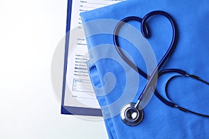 Medical stethoscope twisted in heart shape lying on patient medical history list and blue doctor uniform closeup