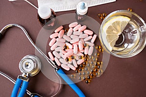 Medical still life: pink pills, fish oil, medical mask, a Cup of water with lemon, stethoscope and medicine in bottles on a brown