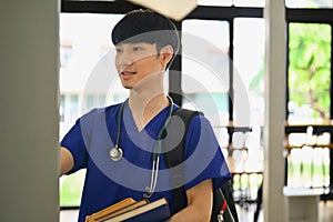 Medical student man wearing blue scrubs with backpack standing at lockers in campus