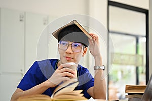 Medical student man wearing blue scrubs putting book on head and looking away. Medical internship concept
