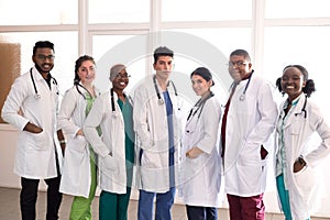 Team of young doctors, mixed race. People of different sex, in white coats, with phonendoscopes, posing, smiling