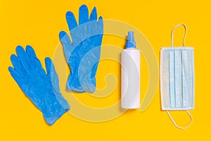 Medical surgical mask, disinfectant or hand sanitizer and blue disposable gloves on yellow background